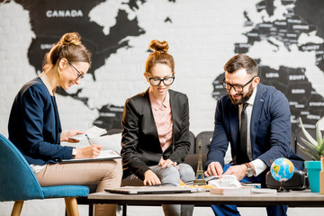 young businesscouple choosing a trip with agent sitting at the travel agency office with world map o