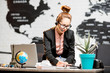 © rh2010 - Portrait of a female travel agent in the suit and headset working indoors on the world map background