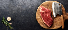Raw Fresh Marbled Meat Black Angus Steak And Meat Cleaver On Wooden Board. Meat On Black Background With Rosemarym Garlic. Copy Space. Top View.