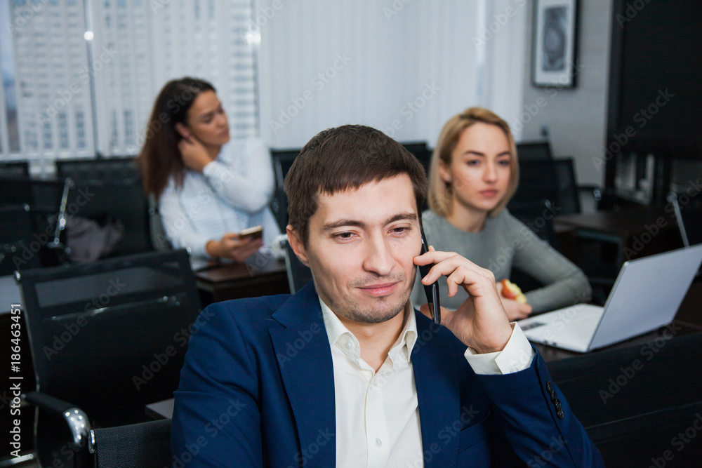Young confident businessman talking by phone at office - obrazy, fototapety, plakaty 