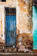 Faded Blue Door Behind Locked Grate On Brick Wall With Broken Plaster