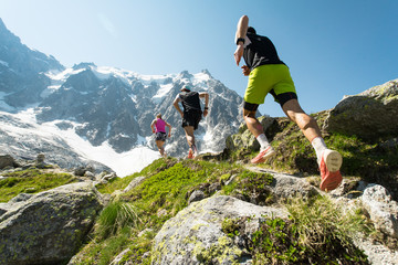 three trail runners, two men and a woman, running up a steep trail in the mountains in the alps on a