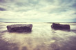 Two rocks on a beach, motion blurred water, peaceful natural background, color toned picture.