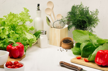 Wall Mural - Kitchen white interior with raw fresh green salad, red cherry tomatoes, kitchenware on soft white wood table, copy space. Spring vitamin dieting food.