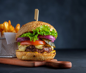 Tasty grilled beef burger with lettuce, cheese and onion served on cutting board on a black wooden table, with copyspace.