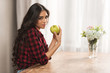 © LIGHTFIELD STUDIOS - beautiful girl in checkered shirt holding green apple and looking at camera at home
