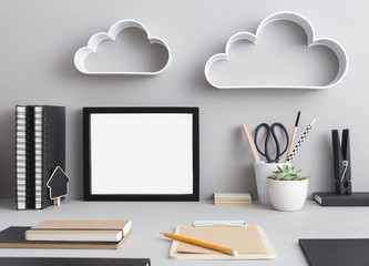 Creative desk with blank picture frame or poster, desk objects, office supplies, books and plant on a gray background. Mock up.