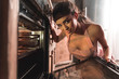 © LIGHTFIELD STUDIOS - sexy young woman in apron opening oven and smiling at camera