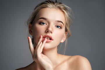 image with beautiful blonde girl touching her lips on grey background. beauty & skin care concept