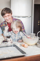 father and child having fun with flour at kitchen while preparing dough