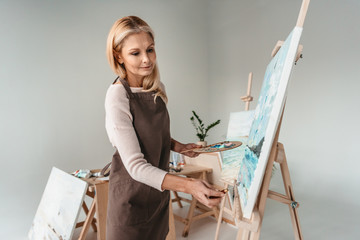 Sticker - beautiful mature woman in apron painting on easel at art class