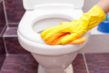 Woman In Yellow Rubber Gloves Cleaning Toilet Seat With Orange Cloth. Bathroom And Toilet Hygiene