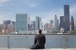 Back view of African American male professional in suits seated in river park across Manhattan, taking in the city skyline