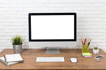 workspace with computer with blank white screen, and office supplies on a wooden desk