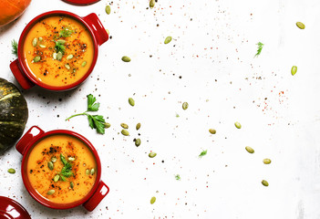 Spicy pumpkin soup puree with spices, herbs and pumpkin seeds in serving pots, gray background, top view