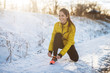 © Dusan Petkovic - Young slim athletic girl tying shoelaces in winter sportswear on snowy winter road with earphones in the sunny morning.