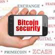 © Maksim Kabakou - Cryptocurrency concept: Hand Holding Smartphone with  red text Bitcoin Security on display,  Tag Cloud background, 3D rendering