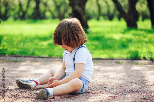Valokuva cute little toddler child boy playing with dirt and sitting on the ground on the
