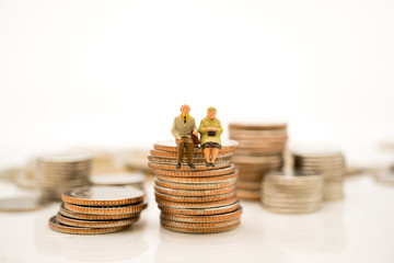 Miniature people, elderly people sitting on stack coins using as job retirement and insurance concept