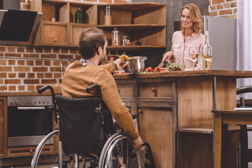 smiling woman with man in wheelchair cooking dinner together at home