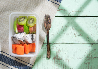 Poster - Mix sliced fruits (papaya,dragon fruit,apple, kiwi) with shadows from a window frame on rustic wooden background