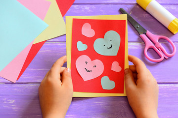 Child is holding a Valentines greeting card in his hands. Child is showing a Valentines greeting card. Simple paper crafts for children concept. Closeup