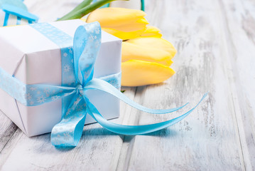 Wall Mural - Gift box with a blue ribbon and bouquet of yellow tulips  on a wooden background