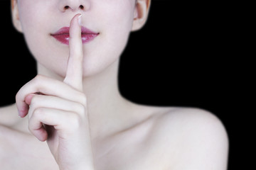  Close up of young woman's face smiling with red lips showing silence gesture on black background - secret concept
