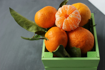 Fresh tangerines with leaves in wooden box on a gray background closeup