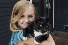 Close-up Portrait Of Girl With Cat Standing Against House