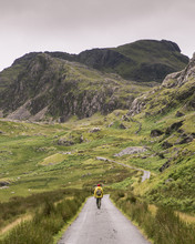 Rear View Of Man With Backpack Walking On Road Amidst Mountains Against Sky