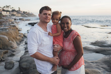 Portrait Of Happy Parents With Daughter At Beach During Sunset