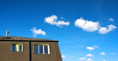 Roof of apartment building with windows on blue sky background.