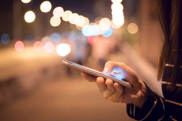 Wall Mural - Close up Hand of woman using Mobile smartphone in the street, night light bokeh Background, copy space.