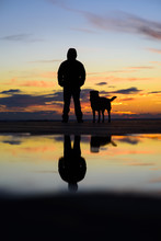 Silhouette Of Man With His Dog At Sunset On Background