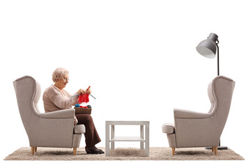 Wall Mural - Lonely elderly woman sitting in an armchair and knitting