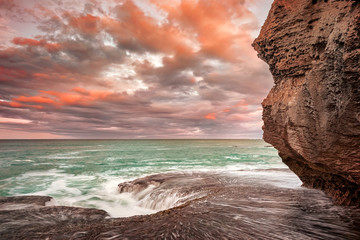 Orange clouds at sunrise over the sea from a sanstone rock shore