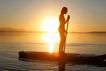 Young Girl Paddle Boarding On Water, At Sunset