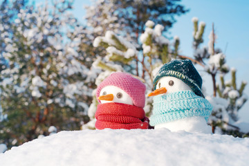 Two small snowmen the girl and the boy in knitted caps and scarfs on snow in the winter. Festive background with a lovely snowman. Christmas card, copy space