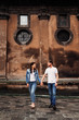 © Ivan - girlfriend and her boyfriend are holding hands and looking at each other against the backdrop of a building with a brown wall