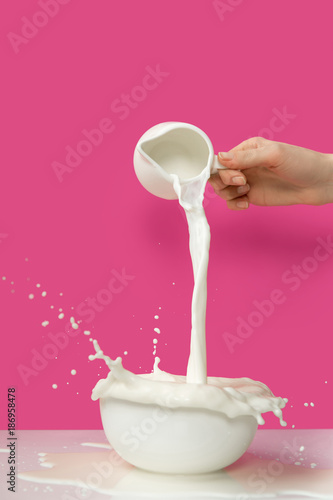 Zdjęcie XXL przycięty strzał osoby odlewania świeże zdrowe mleko z dzbanka do miski na różowo