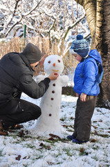 Wall Mural - Father and son make a snowman in backyard. Happy family play on snow