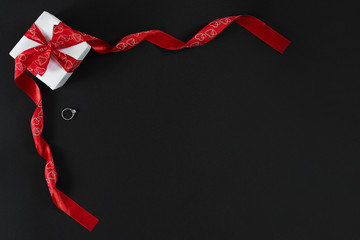 White gift box with red ribbon and ring isolated on black backgr