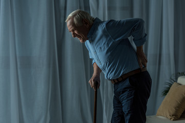 Senior man suffering from back pain leans on a cane