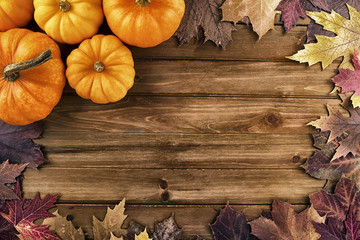 Wall Mural - Pumpkins with fall leaves over wooden background. Top view.