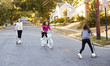 © Monkey Business - Three girls riding on scooters and a bike in the street