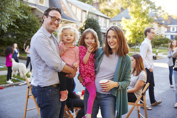 Parents holding young kids smile to camera at a block party