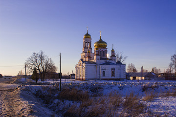 Wall Mural - The Church of the Nativity in the Russian village of Lebyazhye on a winter evening and the dry grass on a snow-covered field.