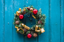 Front View Of A Traditional Christmas Wreath Hung On An Old Wooden Front Door.