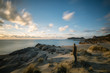 © Leander Nardin/Stocksy - young man standing on a sandy beach looking at the ocean at suns